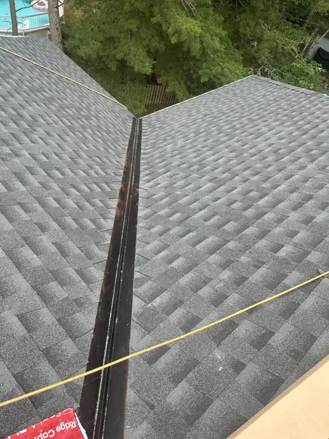 New charcoal architectural shingles along an open black metal roof valley